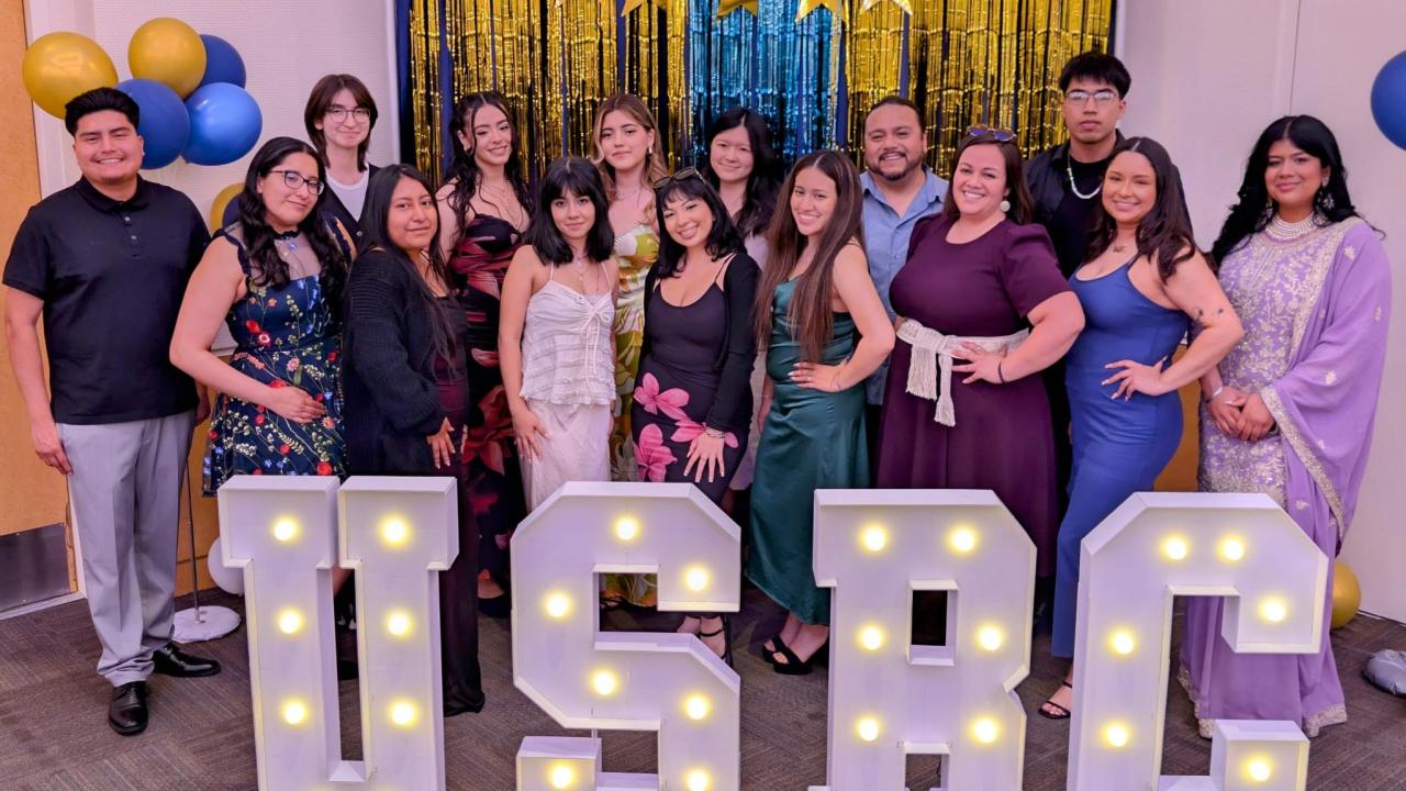 A team photo of USRC team members in at the Center's 10th celebration. Members are standing behind light up letters "USRC".