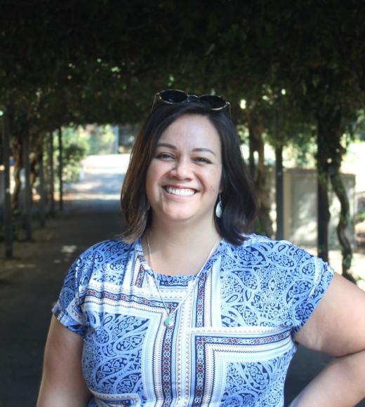 Daniela smiling warmly in front of greenery background.