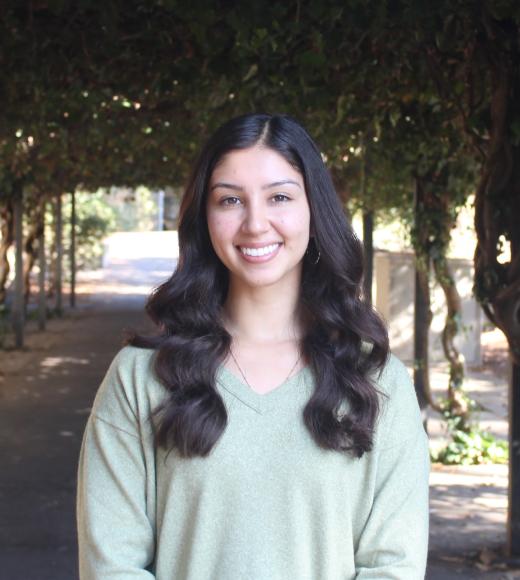Edith smiling warmly into the camera with greenery background.
