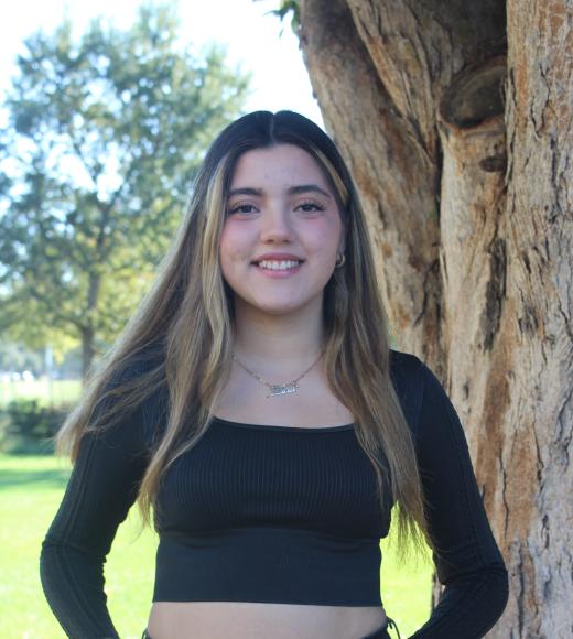 Lucia is standing in front of a tree trunk with greenary background,
